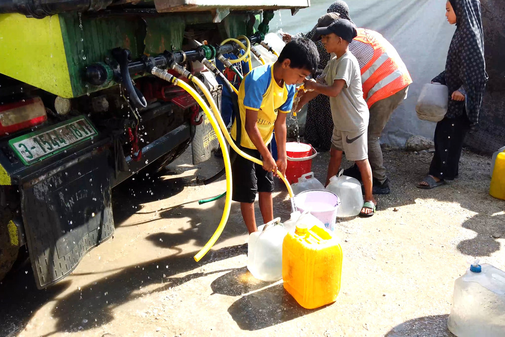 Children collect water from a truck in a displaced persons camp in Gaza.